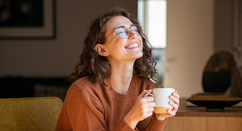 Cheerful woman enjoying coffee after eating a weed chocolate bar.